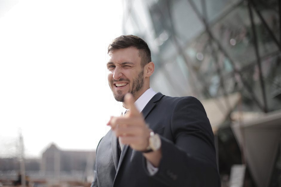 Confident businessman in a suit winking with a smile outdoors, conveying success.